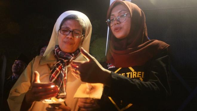 Warga saling membantu menyalakan lilin saat mengikuti aksi solidaritas Malam Seribu Lilin di depan Gereja Katedral, Malang, Jawa Timur, Senin (14/5).