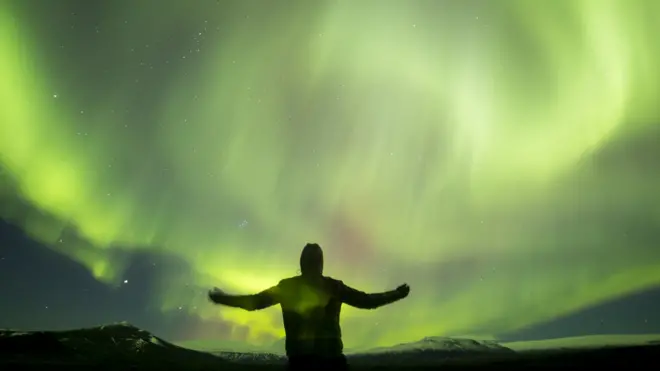 Hombre con brazos abiertos ante una aurora boreal
