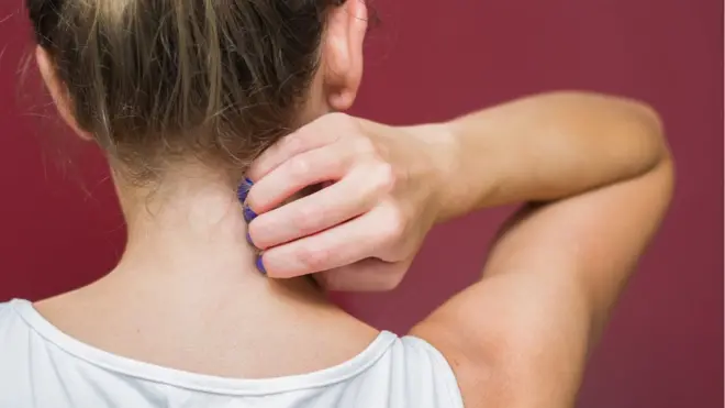 Mujer joven de espaldas rascándose.