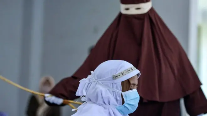 An Indonesian woman is publicly caned as punishment under Aceh province's Sharia laws for being caught with her boyfriend, in March 2021.