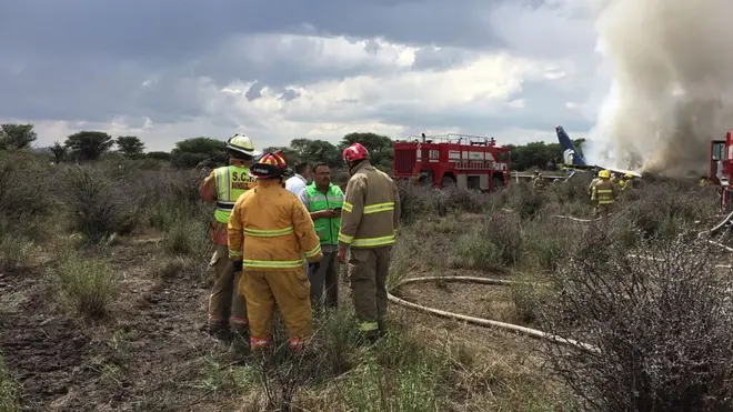 ڈورانگو میں گرنے والے جہاز کے قریب امدادی کارکن موجود ہیں اور عقب میں تباہ ہونے والے جہاز سے دھواں اٹھتے نظر آسکتا ہے
