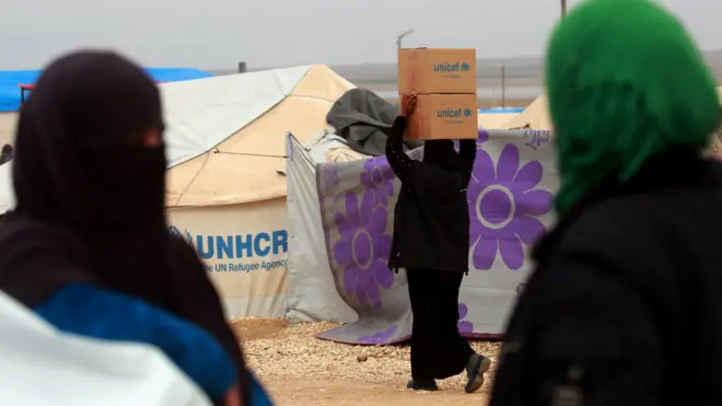 A woman carries boxes of humanitarian aid supplied by Unicef at a refugee camp in Syria's north-eastern Hassakeh province on February 26, 2018