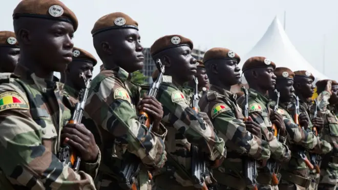 Malian soldiers stand holding rifles and listening to their national anthem during celebrations to mark the country's independence