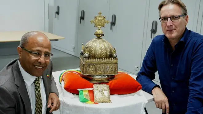 Sirak Asfaw and Arthur Brand sit next to the crown, which depicts the Holy Trinity and Christ's twelve disciples