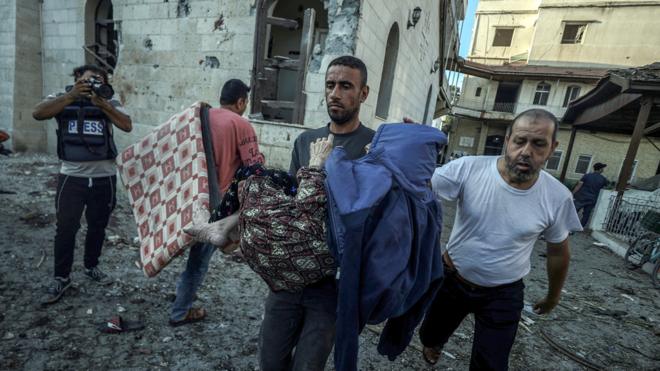 加沙城阿赫利浸信會醫院內一位巴勒斯坦人將一位在空襲中受傷的病患抱離醫院廢墟（18/10/2023）
