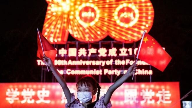 Une fille portant un masque tout en agitant le drapeau national lors du spectacle de lanternes de l'histoire du centenaire de la fondation du PCC au jardin de l'Expo, le 25 juin 2021 à Wuhan, Hubei. Chine
