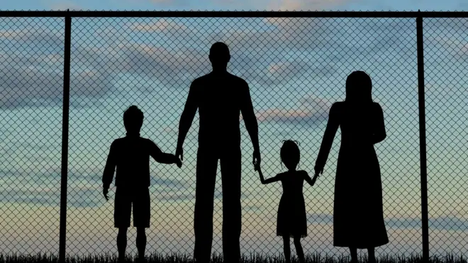 Силуэты семьи на фоне забора из проволоки
