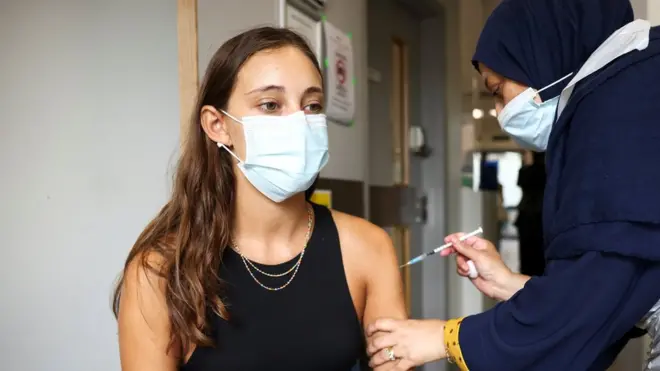 Nurse (health worker) preparing to administer a jab of Pfizer BioNTech Covid vaccine to a young woman (teen,female teenager, teenagers) at Central Middlesex Hospital in London, August 1st 2021.