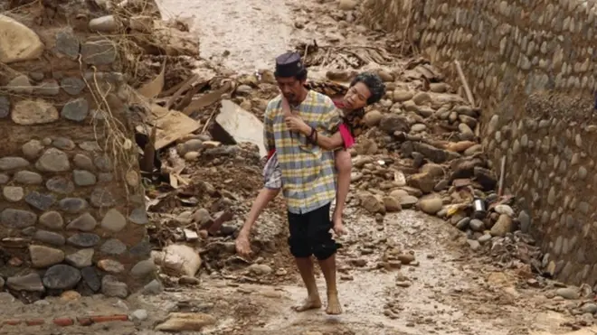 Seorang pria menggendong istrinya yang sedang sakit di tengah kondisi bencana di Desa Sukarame, Kecamatan Sajira, Kabupaten Lebak.