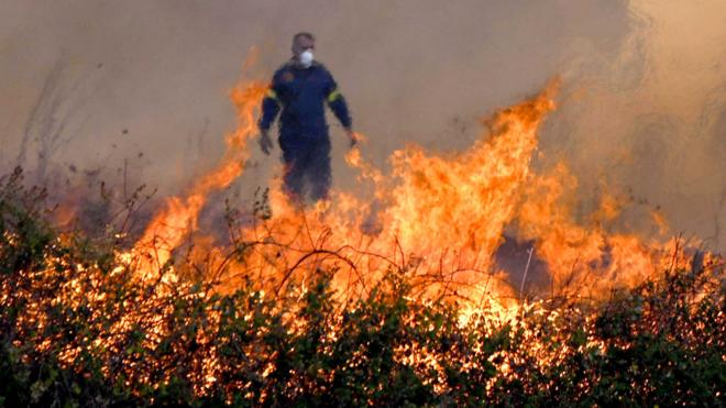 A firefighter stands behind flames during a wildfire in the Avanta area, near Egnatia Odos motorway, in Alexandroupolis, Thrace, northern Greece, on 21 August 2023