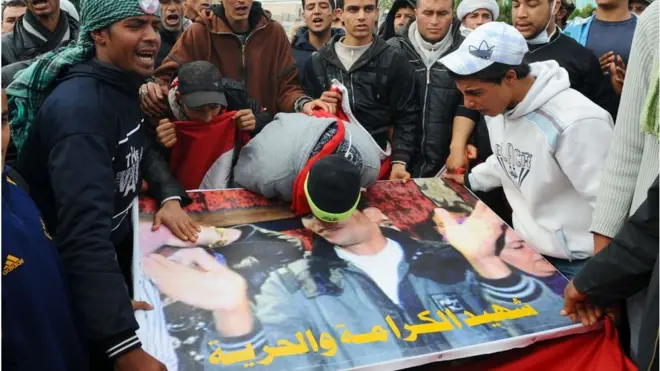 متظاهرون يقبلون صورة محمد البوعزيزي أمام القصر الحكومي في تونس العاصمة في 28 يناير 2011.