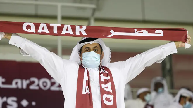 Un homme masqué tient une écharpe de football du Qatar