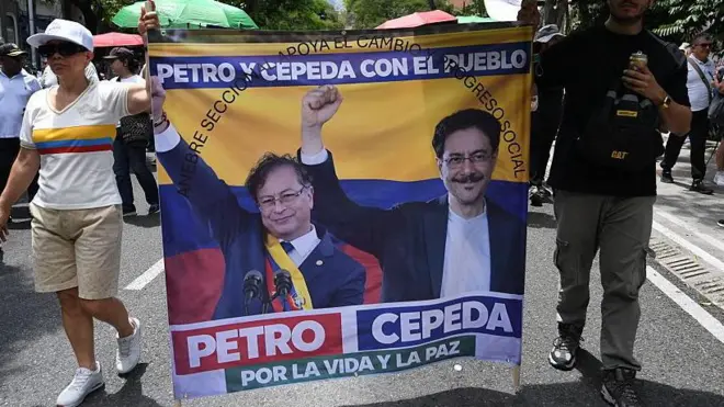 Una mujer y un hombre caminan sosteniendoo una pancarta con la imagen de Gustavo Petro e Iván Cepeda.