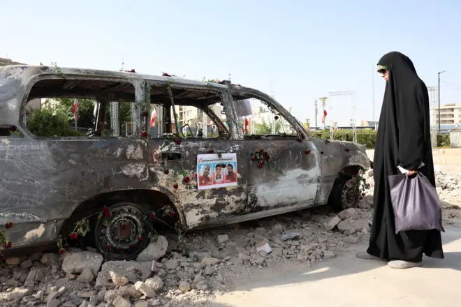 Uma mulher iraniana com véu está ao lado de uma ambulância da Sociedade do Crescente Vermelho Iraniano (IRCS), destruída em um ataque israelense em Teerã, Irã, em 23 de junho de 2025.