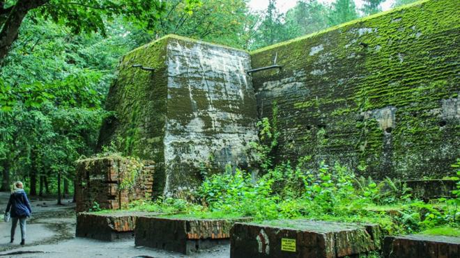 Turista observa monumento coberto por floresta no Wolfsschanze