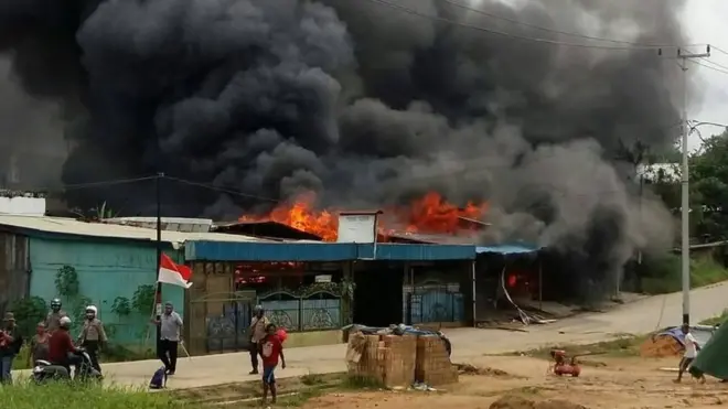Beberapa orang dan anggota polisi berjalan di depan bangunan rumah yang dibakar oleh sekelompok orang di kota Sorong, Papua Barat, Selasa (20/08)