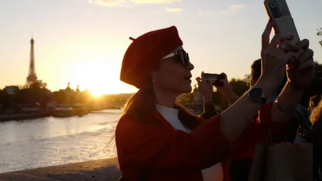 A picture taken on October 8, 2022 in Paris shows people taking pictures at sunset in front of the Eiffel Tower.