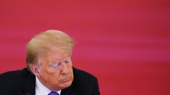Donald Trump cabisbaixo diante de fundo vermelho