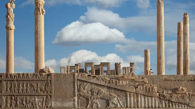 Ruins of Apadana and Tachara Palace behind stairway with bas relief carvings in Persepolis Unesco World Heritage Site against cloudy blue sky in Shiraz, Iran
