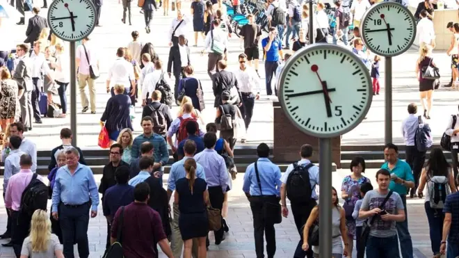 Personas caminando una plaza con varios relojes