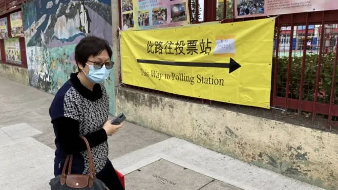 A woman walks past a sign pointing towards a polling station as Hong Kong votes for its legislative council, 19 December 2021