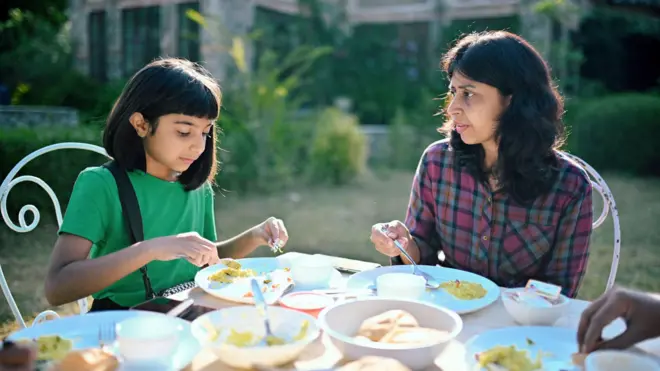 Mother and daughter sitting together and eating breakfast in an open lawn 