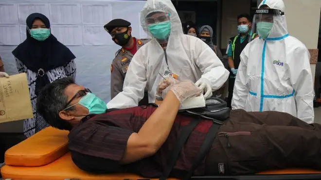 Petugas dengan mengenakan baju hazmat membantu warga menggunakan hak suara saat simulasi pemungutan suara Pilkada Surabaya 2020, di halaman Gapura Surya Nusantara, Pelabuhan Tanjung Perak, Surabaya, Jawa Timur, Senin (30/11). Simulasi tersebut untuk memberikan pemahaman terkait mekanisme dan prosedur proses pemungutan suara dengan menerapkan protokol kesehatan di tengah pandemi Covid-19.
