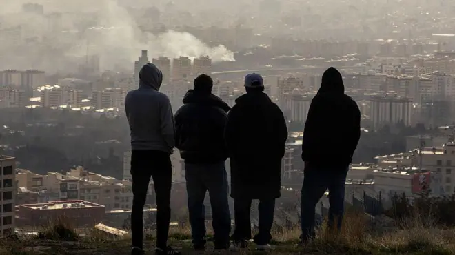 Unos hombres observan cómo se eleva una columna de humo tras una explosión, el 2 de marzo de 2026, en Teherán, Irán. 
