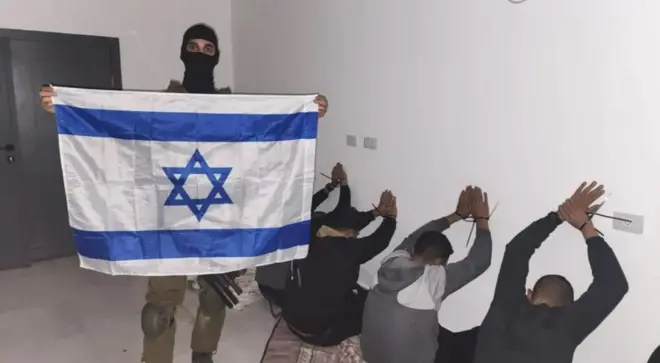 An Israeli soldier posts a photo of detainees while holding an Israeli flag