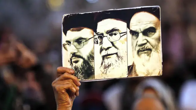 متظاهر إيراني يحمل صورة تجمع المرشد الأعلى الإيراني السابق آية الله روح الله الخميني (يمين)، والمرشد الأعلى الإيراني الحالي آية الله علي خامنئي (وسط)، والأمين العام لحزب الله حسن نصر الله (يسار)