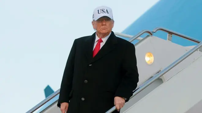 Trump, na escada do avião, usando um boné escrito USA