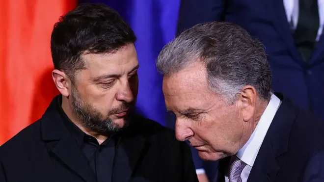 الرئيس الأوكراني فولوديمير زيلينسكي (يسار) والمبعوث الأمريكي الخاص ستيف ويتكوف يتحدثان. زيلنسكي يرتدي قميصاً أسود وجاكيت بنفس اللون، بينما يرتدي ويتكوف بدلة رسمية تبدو سوداء مع قميص أبيض وربطة عنق تبدو باللونين الفضي والأسود.