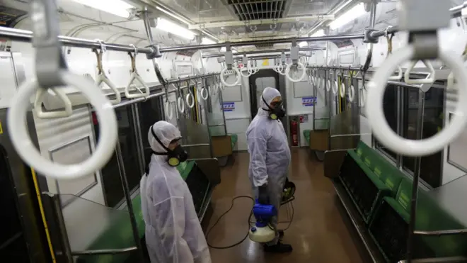 Petugas berseragam tertutup menyemprotkan disinfektan di KRL