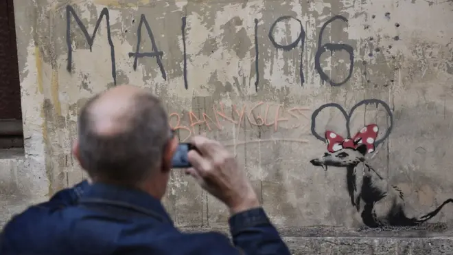 Čovek fotografiše mural za koji se veruje da je Benksijev, na kojem se vidi pacov sa mašnom Mini Maus i natpisom „Maj 1968.“