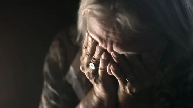 Mulher idosa triste, com as mãoes no rosto
