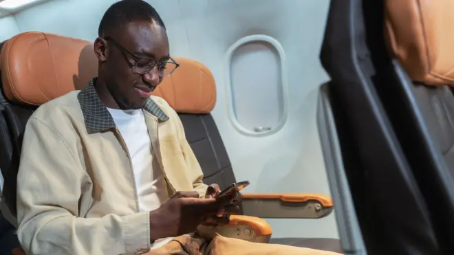 Stock image of pesin iside plane dey operate phone