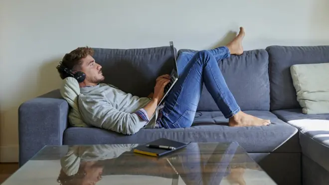 Un hombre trabajando en el sofá de su casa.