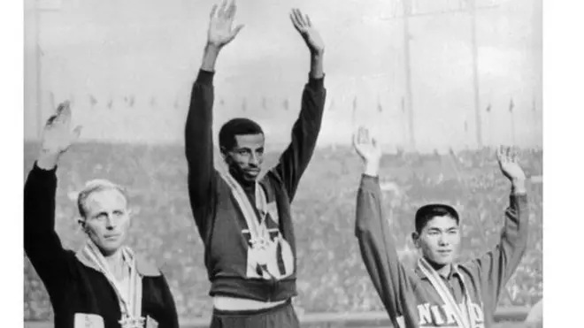 ኣብ 23 ጥቅምቲ 1964 ኣብ ቶኢክዮ ኣብ ዝተካየደ ኦሎምፒክ ኣበበ ቢቂላ ቀዳማእ ወጺኡ ወርቂ መዳልያ ኣብ ዝተሸለመሉ ምስ ብርጣንያዊኡ ባሲል ሄትልይ (ጸጋማይ) ከምኡ እውን ምስ ጃፓናዊ ኮኩቺ ቱባርያ (የማናይ)