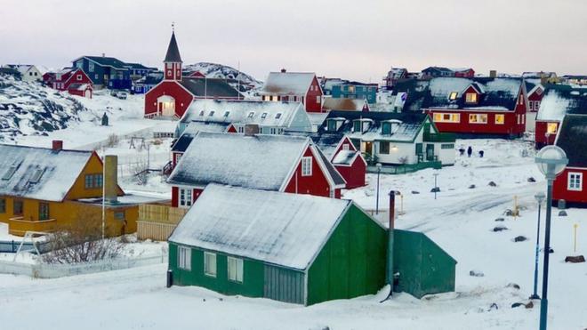A town in typical Greenland style is pictured - brightly-painted wooden walls and triangular roofs covered in snow are the main features of these sparsely dotted homes