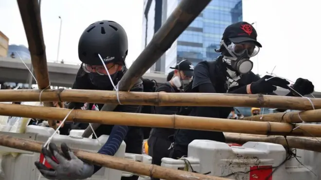 Люди в касках и респираторах связывают бамбуковые шесты