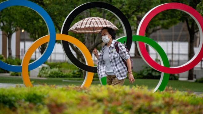 Uma mulher segura um guarda-chuva passando pelos anéis olímpicos em frente ao Museu Olímpico do Japão em Tóquio