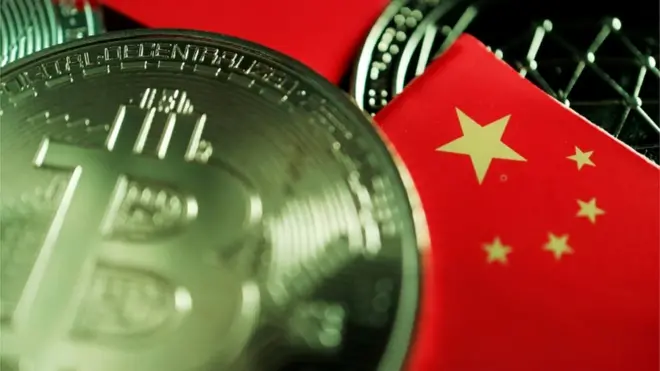 Une pièce de monnaie du monde réel portant le logo du bitcoin est éparpillée sur une table au milieu de drapeaux chinois miniatures.
