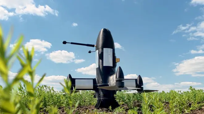 A P1-SUN Ukrainian interceptor drone sits in a green field under a blue sky. It's a black, bullet-shaped drone with four propellers at its base