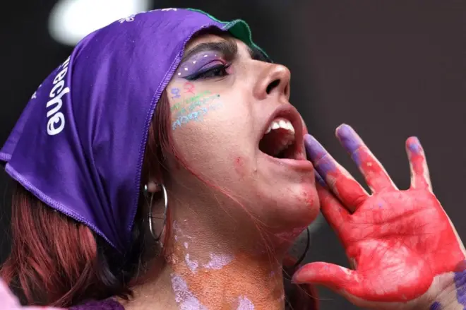 Mor bir bandana takmış bir kadın slogan atarken. 