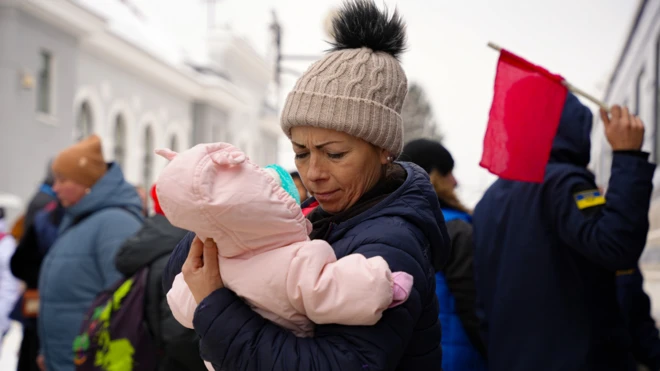 Жінка тримає маленьку дитину на тлі поїзду