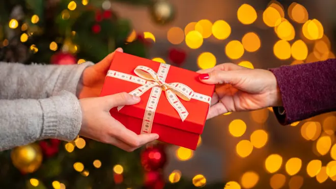 Two hands passing a red gift box with a bow to another hand