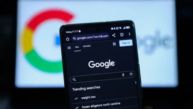 telefone celular no qual aparece um mecanismona czym polega freebetbusca Google. O logotipo da empresa aparecena czym polega freebetum computador atrás