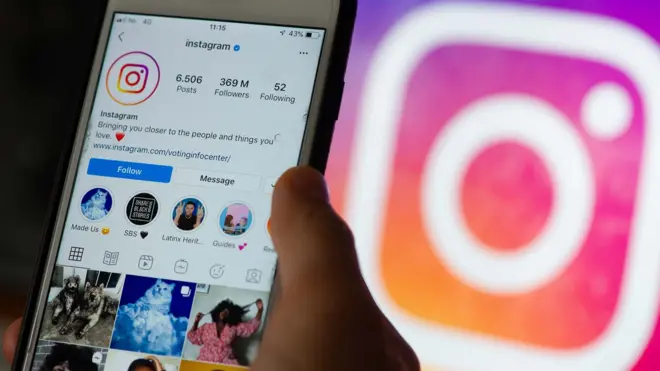 Ekran smartfona pokazujący platformę społecznościową Instagram i dłoń trzymająca telefon z logo Instagrama w tle