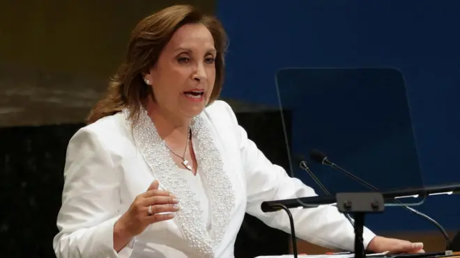 Dina Boluarte, presidenta de Perú, vestida de blanco, habla desde un estrado