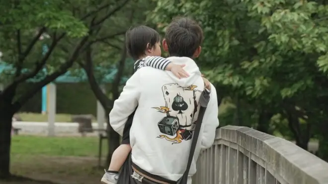 一名身穿連帽衫的男子抱著嬰兒走過公園裡的一座橋